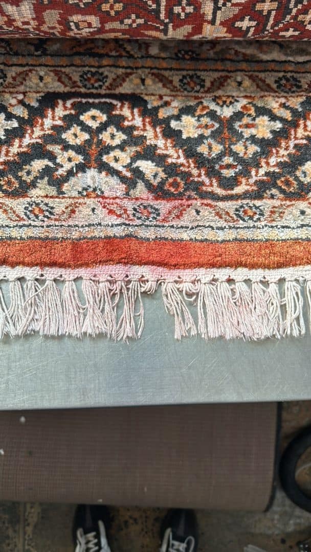 Image showing a rug with dye bleed on its fringe placed on a metal surface.