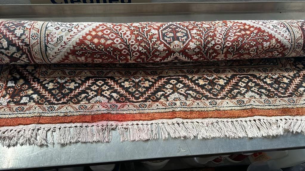 Rolled-up rug with dye bleed on fringe placed on a metal surface.