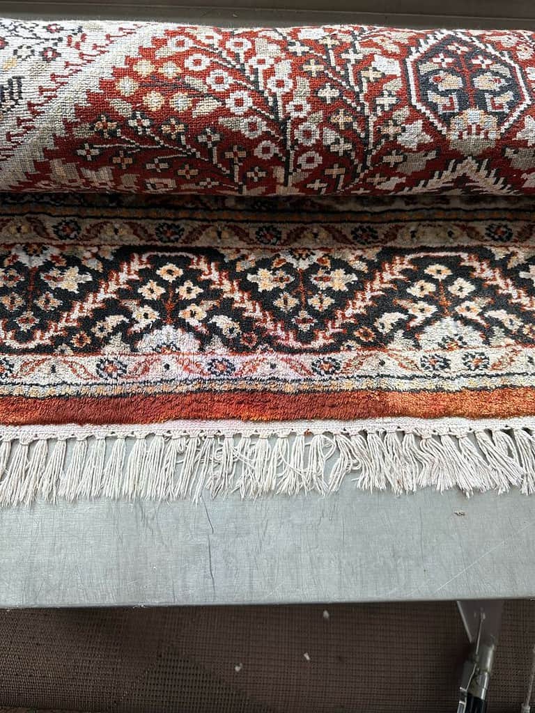 Rolled-up patterned rug with dye bleed on the fringe placed on a metal surface.