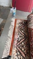 Image of a rug with dye bleed on the fringe alongside cleaning tools in a workshop.