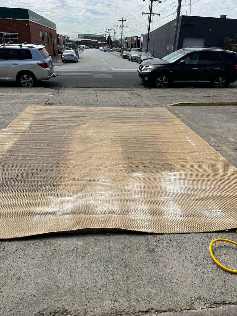 Jute rug on concrete with cleaning powder, surrounded by cars and buildings.