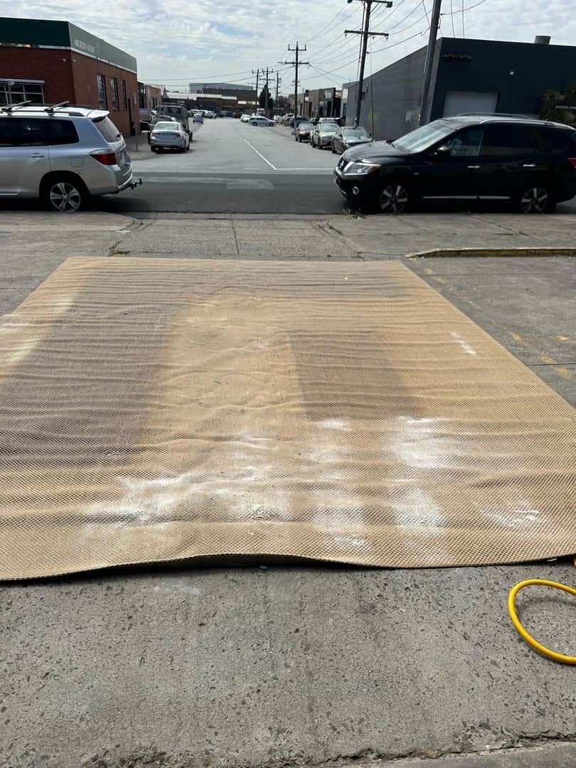 Jute rug on concrete with cleaning powder, surrounded by cars and buildings.