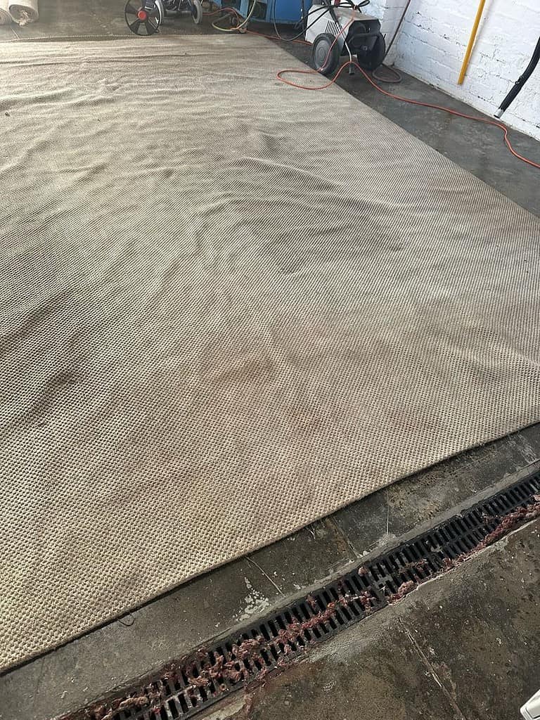 Jute rug on concrete floor with cleaning equipment and drainage grate visible.