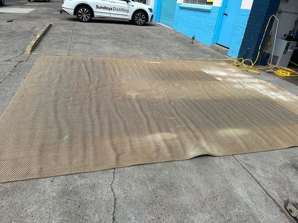 Jute rug on concrete with discoloration, near a branded vehicle and cleaning equipment.