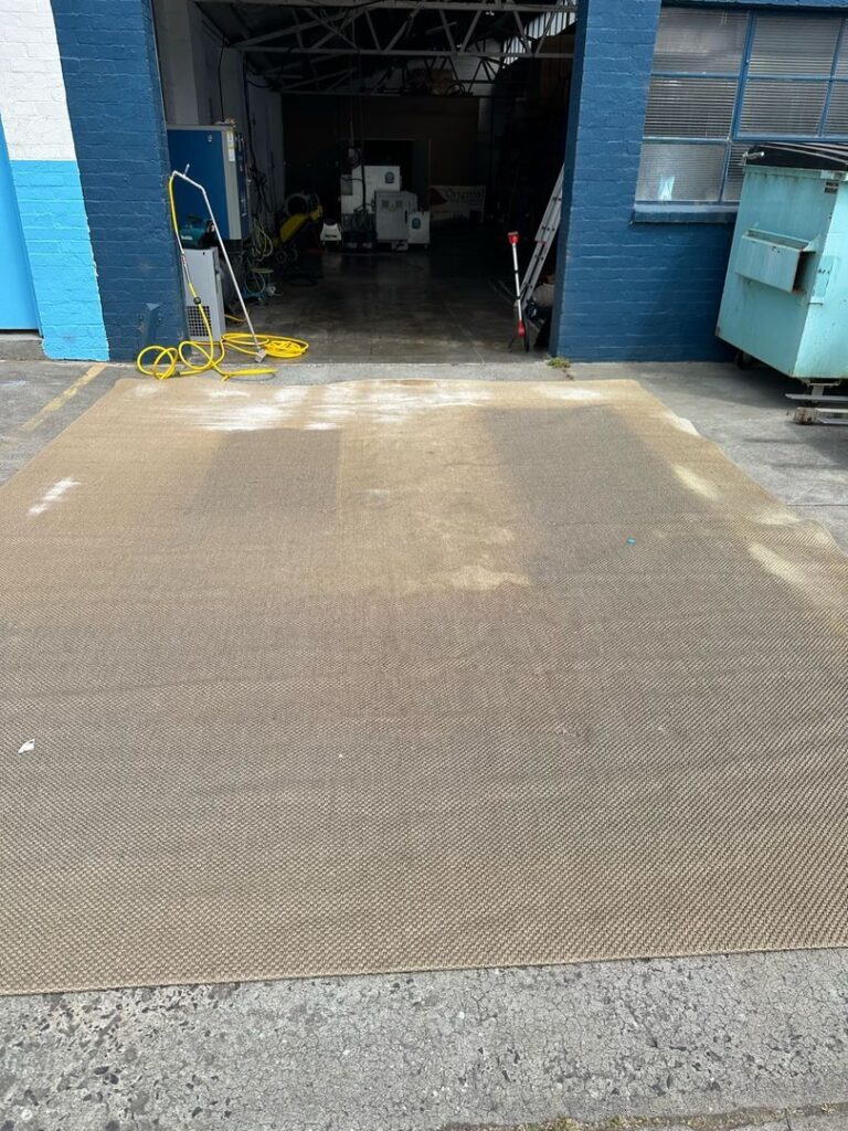 Jute rug on concrete with cleaning equipment nearby at an industrial site.