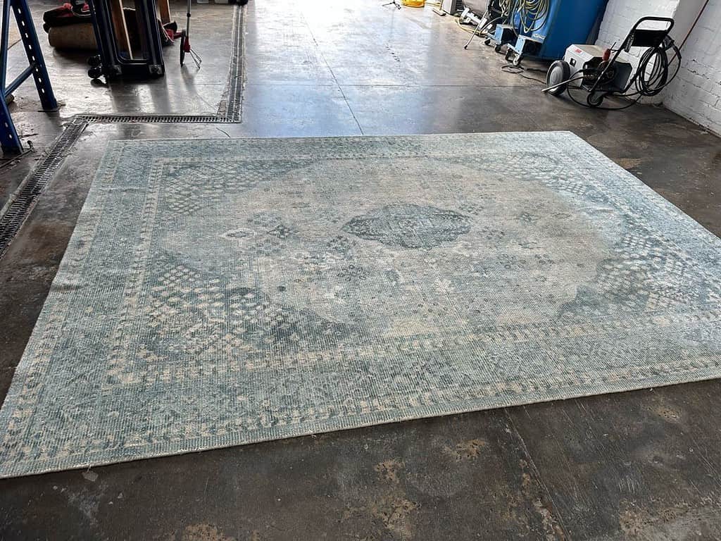 Patterned rug on concrete floor in workshop with equipment around.
