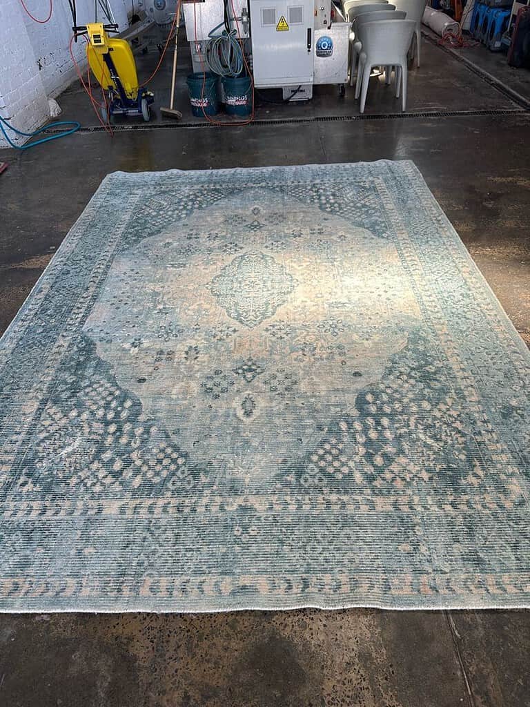 Image of a patterned viscous and wool mix rug in a cleaning facility with industrial equipment in the background.