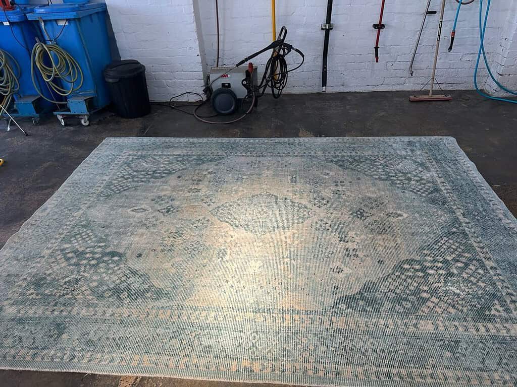 A patterned viscous and wool rug on a concrete floor in a cleaning facility.