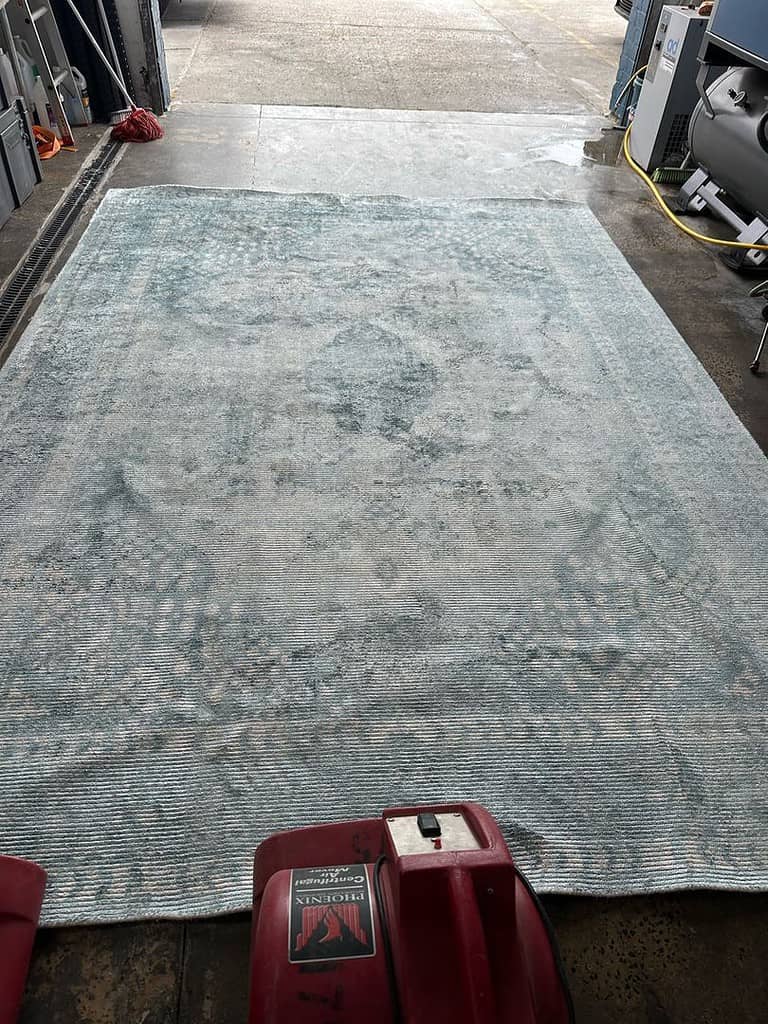 Large rug on concrete floor with Phoenix cleaning machine in an industrial environment.