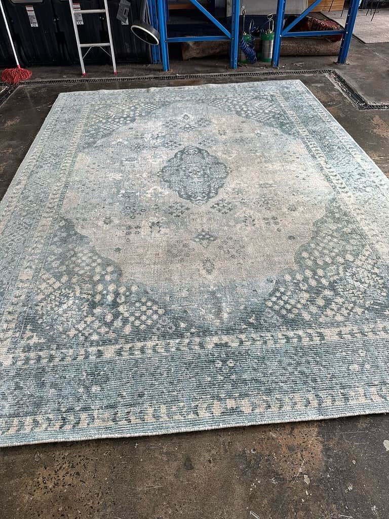 Viscous Wool Mix Rug in Industrial Setting Image of a patterned rug in shades of blue and grey on a concrete floor in an industrial area.