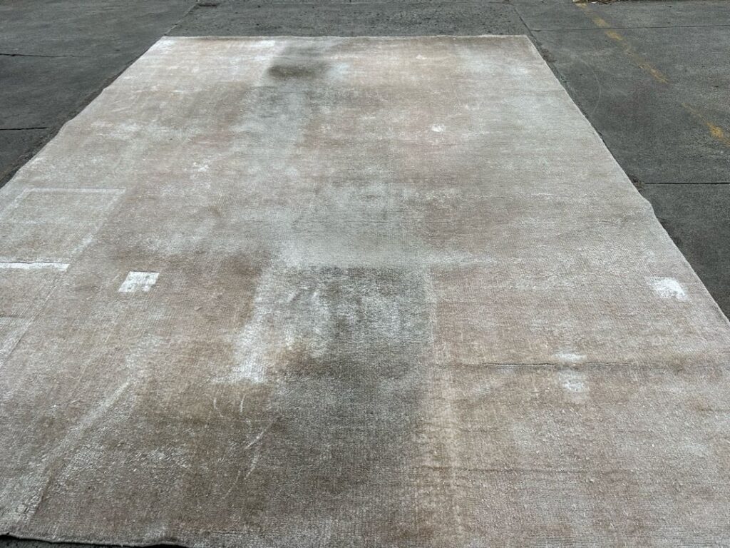 Large rug on concrete surface with visible discoloration and wear.