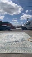 Rug with viscous and wool mix pattern laid out in an outdoor area with cars, utility poles, and a partly cloudy sky.