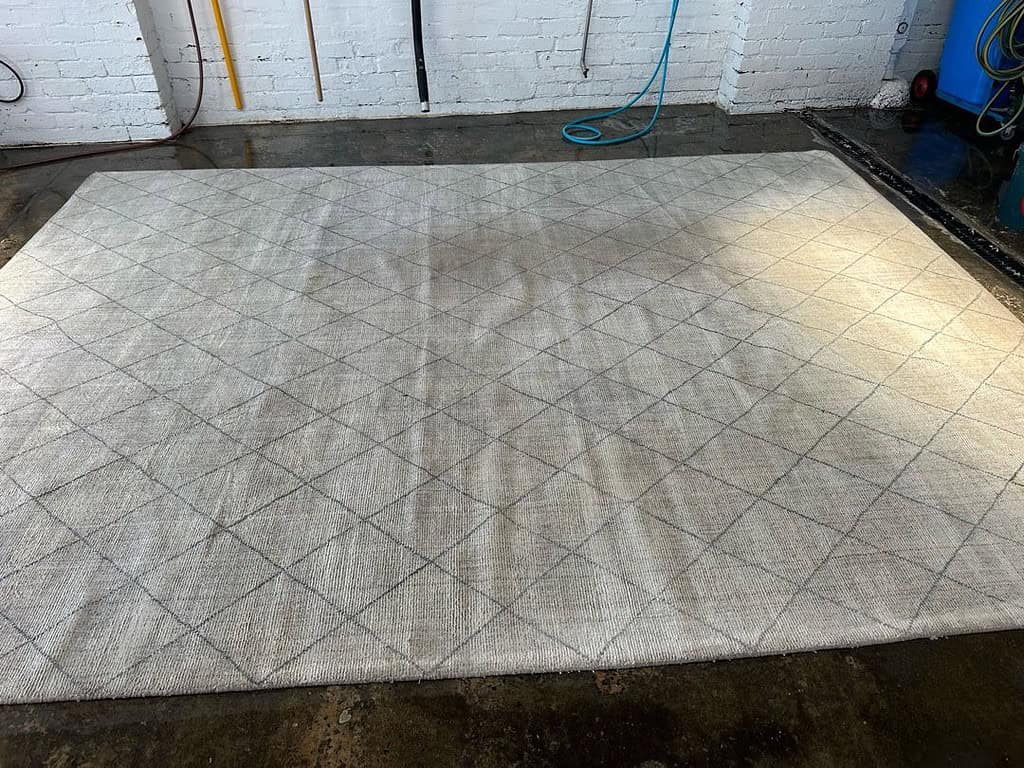 Large diamond-patterned rug in an industrial cleaning area with tools nearby.