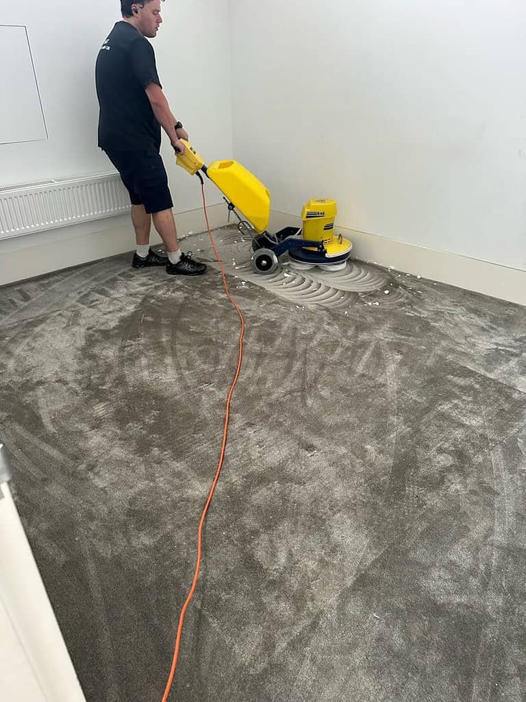 Person cleaning plush carpet with a yellow machine in a white-walled room.