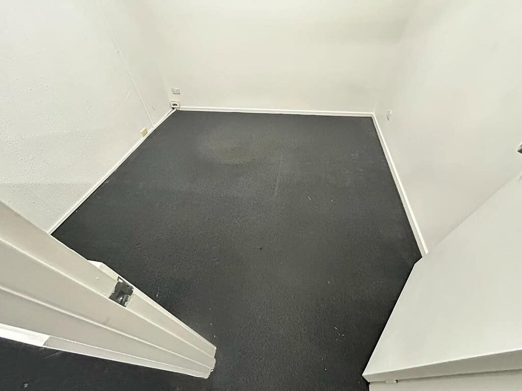 Empty office room with clean dark carpet and white walls.