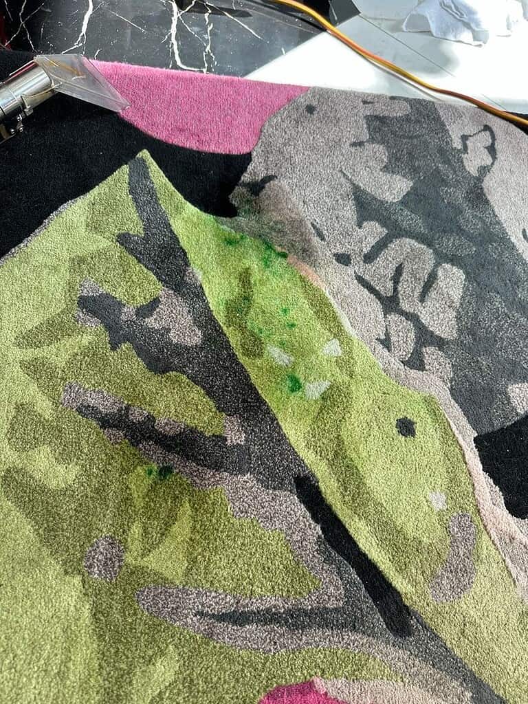 Carpet Stain Removal Process Image of a colorful carpet with green stains being cleaned by a tool.